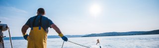 Man on a boat with yellow trousers dragging up fishing gear in the sun